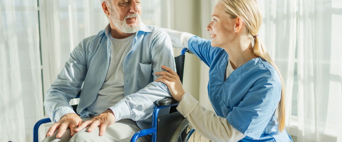 Pflegekraft unterhält sich mit Pflegeperson im Rollstuhl, verlinkt zum Blogbeitrag Pflegerente versus Pflegetagegeld