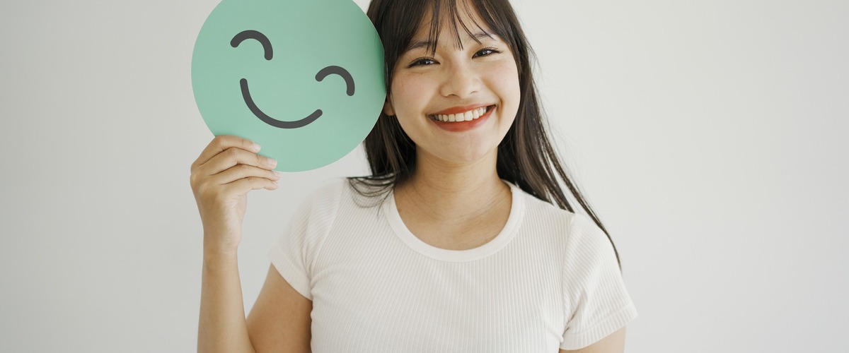 Bild zeigt eine lächelnde Frau mit Papier Smiley in der Hand verlinkt zum Blogbeitrag BU- und Grundfähigkeits-Versicherung
